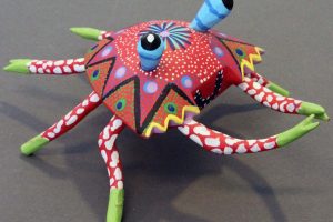 Alibrejes wood carving with dots Alebrije wooden carving of a fantastical red creature with blue horns, green legs, and dotted patterns, representing traditional Mexican folk art.