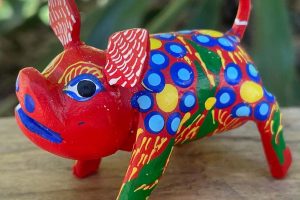 Alibrejes wood carving with painted lines and dots Alebrije-style wooden pig sculpture painted with bright red, blue, and green dots and geometric shapes.