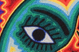 Intricate huichol-yarn-painting with that signature I see your soul eye Close-up detail of a Huichol yarn painting showing an intricate green eye pattern made from layered threads.